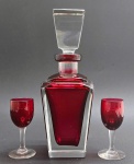 01 licoreira com tampa e corpo retangulares e facetados, e 02 taças de licor com detalhes ovais; em cristal incolor e na cor rubi. Medidas: 26 x 9 cm; 10,5 x 4,5 cm. Base da tampa da licoreira com ínfimo bicado; vértices na parte superior do corpo da licoreira com ínfimo bicado.