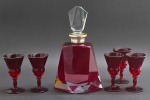 01 licoreira em cristal incolor e na cor rubi, com tampa e corpo geométricos e facetados, e 05 taças com corpo no estilo trompete em vidro rubi; bocal da licoreira em metal espessurado à prata. Medidas: 26 x 14 cm; 11 x 6 cm . Licoreira com dois ínfimos bicados.