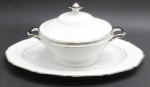CT TIELSCH ALTWASSER, GERMANY - Parte de serviço de jantar com 01 terrina circular e 01 travessa oval, em porcelana alemã; pega da tampa e alças da terrina, faixas e filetes adornados na cor prata. Marca da manufatura na base. Numerados. Medidas: 29 x 18 cm; 42 x 28 cm.