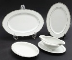 CT TIELSCH ALTWASSER, GERMANY - Parte de serviço de jantar com 03 travessas ovais de diferentes tamanhos e 01 molheira com presentoir integrado; em porcelana alemã; faixas e filetes adornados na cor prata. Marca da manufatura na base. Numerados. Medidas: 32 x 21 cm; 22 x 14 cm. Faixa e filetes prata das travessas menor e média ligeiramente desvanecidos.