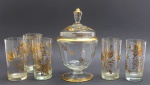 01 bomboniere e 05 copos cilíndricos em cristal translúcido; com diferentes padrões decorativos que incluem motivos florais, vegetalistas, faixas e filetes em dourado. Medidas: 25 x 14 cm; 14 x 7 cm. Douração ligeiramente desvanecida em alguns locais das peças, base da tampa da bomboniere com ínfimo bicado.