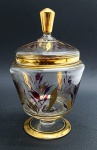Bomboniere em cristal translúcido adornado com faixas e filetes dourados, e motivos vegetalistas em vermelho e dourado. Pega da tampa com douração total; base pedestal. Medidas: 26 x 15 cm. Borda com ínfimo bicado; douração desvanecida em alguns pequenos pontos da peça.