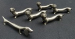 06 suportes de mesa para talheres, em metal espessurado à prata, com a representação de cães da raça Dachshund, sendo cinco no mesmo modelo, e um com modelo que difere dos demais. Medidas: 6,5 x 3 cm; 9 x 2,5 cm.