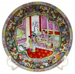Prato decorativo de temática oriental, decorado com chaves gregas, elementos florais e vegetalistas, e cena com personagens em trajes tradicionais em sua galeria central. Em porcelana multicolorida com detalhes em dourado. Fabricação chinesa. Medidas: 27 cm (diâm.).