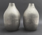 WOLFF - Par de vasos em metal, com borda estreita e corpo abaulado, trabalhado com ranhuras paralelas. Medidas: 30 x 18 cm. Com ínfimos pontos amassados.