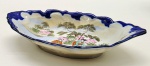 Travessa de temática oriental, no formato oval, com borda recortada em azul cobalto e galeria central adornada com gueixas em ambiente campestre. Em porcelana multicolorida. Fabricada no Japão. Medidas: 20 x 12 cm.