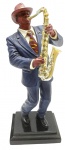 Escultura com a representação de um músico tocando saxofone; em resina policromada sobre base retangular escalonada e laqueada. Medidas: 28 x 12 x 9 cm. Saxofone com desgastes na pintura; alguns dedos com danos; boca com resíduo de cola.