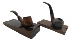 CACHIMBOS - Lote com 2 cachimbos em madeira, artesanais. Um no estilo terroso com piteira em baquelite preta e o outro com piteira em baquelite marmorizado. Acompanham porta cachimbos. Medida: 15cm aproximadamente cada. Contém marcas, desgastes, pequenos arranhões e porta cachimbos aleatórios (podem ou não ser dos respectivos cachimbos do lote).