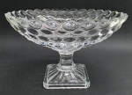 Centro de mesa com borda ondulada e amplo bojo com elementos ovais em relevo; base quadrangular tipo pedestal, com haste facetada e detalhes canelados; em cristal translúcido. Medidas: 30 x 19 cm.