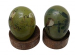 Par de antigos ovos orientais em jade, assinados, e decorados à mão com delicados e coloridos motivos de pássaros; apoiados sobre base circular de madeira. Medidas: 4 x 3 cm.