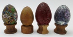 04 ovos decorativos com diferentes materiais e acabamentos, sendo um vermelho em madeira laqueada tipo cinábrio, um metal esmaltado com coloridos desenhos florais em cloisonné, um revestido em madrepérola, e um de percussão, em madeira polida com a função de chocalho; apoiados em bases individuais de madeira torneada. Medidas: 6 x 5 cm; 5 x 4 cm.