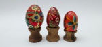 03 ovos decorativos em madeira policromada, adornados à mão com diferentes padrões florais, sendo um deles com detalhes hexagonais; apoiados em bases individuais de madeira torneada. Medidas: 6 x 5 cm; 5 x 4 cm.