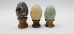 03 diferentes ovos decorativos em rochas lapidadas e polidas; apoiados em bases individuais de madeira torneada. Medidas: 6 x 5 cm; 5 x 4 cm.