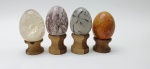 04 diferentes ovos decorativos em rochas lapidadas e polidas; apoiados em bases individuais de madeira torneada. Medidas: 6 x 5 cm; 5 x 4 cm. Ovo maior com ínfimo lascado no topo; um dos ovos com ínfimos pontos trincados.