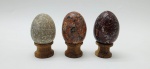 03 diferentes ovos decorativos em rochas lapidadas e polidas; apoiados em bases individuais de madeira torneada. Medidas: 6 x 5 cm; 5 x 4 cm.