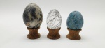 03 diferentes ovos decorativos em rochas lapidadas e polidas; apoiados em bases individuais de madeira torneada. Medidas: 6 x 5 cm; 5 x 4 cm.
