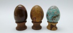 03 diferentes ovos decorativos em rochas lapidadas e polidas; apoiados em bases individuais de madeira torneada. Medidas: 6 x 5 cm.