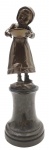 Antiga escultura com a representação de uma menina em trajes camponeses de época e segurando uma tigela; em bronze, apoiada sobre pedestal de mármore torneado. Medidas: 24 x 9 cm.