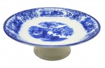 FLOW BLUE - SHANGHAI W. H. GRINDLEY & CO. LTD., ENGLAND - 01 prato pedestal de porcelana para bolos/doce, em Flow Blue, padrão de decoração Shangai, com ilustração pictórica clássica inspirada em paisagens asiáticas tradicionais, geralmente com construções pagodes, pontes, árvores estilizadas e figuras. "Flow Blue" (ou azul fluido) é um estilo clássico de cerâmica e porcelana antiga do século XIX, famoso por seu padrão azul-cobalto que se "espalha" e borra intencionalmente sobre o fundo branco durante a queima. O padrão "Shanghai" produzido pela manufatura inglesa W. H. Grindley & Co. é um dos designs mais célebres e colecionáveis dentro do estilo flow blue (azul fluido). Introduzido originalmente no final da era vitoriana, por volta de 1891 e produzido até 1914, ele exemplifica a forte influência do estilo Chinoiserie (orientalismo) na Europa da época. Medidas: 25 x 9,5 cm.