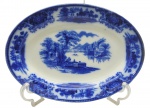 FLOW BLUE - SHANGHAI W. H. GRINDLEY & CO. LTD., ENGLAND - 01 travessa oval de porcelana, em Flow Blue, padrão de decoração Shangai, com ilustração pictórica clássica inspirada em paisagens asiáticas tradicionais, geralmente com construções pagodes, pontes, árvores estilizadas e figuras. "Flow Blue" (ou azul fluido) é um estilo clássico de cerâmica e porcelana antiga do século XIX, famoso por seu padrão azul-cobalto que se "espalha" e borra intencionalmente sobre o fundo branco durante a queima. O padrão "Shanghai" produzido pela manufatura inglesa W. H. Grindley & Co. é um dos designs mais célebres e colecionáveis dentro do estilo flow blue (azul fluido). Introduzido originalmente no final da era vitoriana, por volta de 1891 e produzido até 1914, ele exemplifica a forte influência do estilo Chinoiserie (orientalismo) na Europa da época. Medidas: 30 x 22 cm.