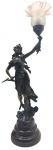 Antiga luminária de mesa escultórica, no estilo Art Nouveau, retratando uma figura feminina em trajes clássicos e esvoaçantes; estruturada em liga de zinco fundida (spelter), muito utilizada no final do século XIX e início do século XX, e patinada na cor marrom escura. Cúpula no formato floral, em vidro fosco. Base circular em metal. Medidas: 85 x 21 cm. Não testada. Com alguns ínfimos pontos de desgaste na pátina.