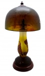 LUIZ OCTÁVIO RAVAGNANI (1962) - Abajur de mesa de inspiração Art Nouveau, no formato cogumelo ("mushroom lamp"); cúpula em domo, em tons castanhos, adornada com cenário campestre, silhuetas de árvores e um cavalo; haste ovalada adornada com motivos fitomórficos marrons sobre fundo amarelo; em pasta de vidro com gravação a ácido; sobre base circular de metal; haste assinada pelo artista RAVAGNANI, mestre vidreiro brasileiro nascido em Petrópolis. Medidas: 42 x 22 cm. Cúpula adaptada posteriormente, mantendo-se a integridade estética do conjunto. Não testado. Base da cúpula com ínfimos bicados.