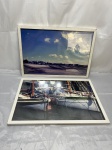 Par de quadros com fotografias de temática náutica, apresentando uma vista panorâmica de porto com vilarejo ao fundo e detalhe de embarcações de pesca com tripulação, protegidos por vidro em molduras de madeira na cor branca. Medindo a moldura 47,5cm x 33cm.