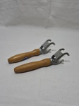Par de pegadores de assadeira em metal com pega em madeira. Medindo 23cm de comprimento.