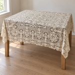 Grande toalha de mesa de tradição madeirense, executada em tecido claro com extensa composição de renda e bordado manual, medindo 2,30 x 1,90 m. Apresenta campo central retangular com reservas circulares, motivos florais e folhagens, cercado por larga barra rendada de desenho contínuo e acabamento recortado.