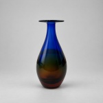 MURANO -Belíssimo vaso em vidro artístico de Murano, medindo 21 x 9 cm. Apresenta corpo bojudo de formato alongado, base estreita e pescoço alto, finalizado por ampla borda circular achatada. Sua composição cromática combina azul-cobalto intenso na parte superior com gradações de verde, âmbar e castanho na região inferior, criando efeitos de profundidade, brilho e transparência conforme a incidência da luz.