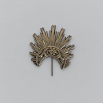 Resplendor em prata de lei trabalhada, com composição radial de raios em diferentes comprimentos e elemento inferior em meia-lua ornamentado por motivos florais e volutas em relevo. Medindo 8 x 7 cm, apresenta haste posterior para fixação.