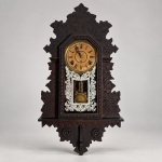 WM. L. GILBERT CLOCK CO.  Relógio mecânico americano modelo OXFORD, conforme etiqueta original preservada no verso, manufaturado em Winsted, Connecticut, Estados Unidos, na virada do século XIX para o XX.Medidas: 72  36  10 cm.Caixa arquitetônica em madeira escura, ricamente recortada e entalhada com motivos florais e folhagens, apresentando mostrador circular com algarismos romanos, moldura metálica e porta frontal envidraçada. A seção inferior do vidro recebe elaborada decoração branca de motivos florais e vegetalistas, enquadrando a visualização do pêndulo.Movimento mecânico de corda com dois pontos de carga, acompanhado de pêndulo e chave de corda. O pêndulo apresenta bob circular em metal decorado com padrão floral estampado. A denominação Wm. L. Gilbert Clock Co. corresponde à empresa reorganizada em Winsted em 1871, importante fabricante da indústria relojoeira de Connecticut. Architectural TrustNo verso permanece a etiqueta original amarela OXFORD  Manufactured by Wm. L. Gilbert Clock Co., Winsted, Conn., U.S.A., elemento particularmente importante para identificação do modelo. Conserva ainda etiqueta brasileira de assistência técnica datada de 05/2005.