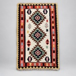 00410 Tapete Kilim indiano, confeccionado em lã sobre lã. Medindo: 1,62 x 1,03, apresenta campo central creme com três grandes medalhões escalonados, acompanhados por pequenos motivos abstratos distribuídos de maneira regular. Barras formadas por faixas geométricas em terracota, preto e amarelo, complementadas por detalhes em verde, rosa, azul-claro e marrom.