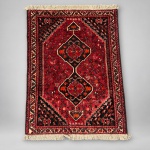 00842 Tapete persa Shiraz, com composição tribal formada por dois grandes medalhões geométricos sobre campo vermelho. Medindo 2,57  1,74 m, apresenta rica ornamentação de pequenos motivos florais e zoomórficos, cercadura em múltiplas faixas e paleta dominada por vermelho, vinho, preto, creme e laranja.