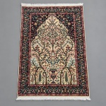 ISFAHAN  Tapete persa de nó manual, apresentando composição vertical do tipo Árvore da Vida, desenvolvida sobre campo marfim com profusa ornamentação vegetal e floral.Medidas: 1,88  1,20 m.A composição parte de vaso central na região inferior, do qual se desenvolvem troncos e ramagens simétricas entre ciprestes, flores, folhagens e aves, culminando em desenho arqueado de caráter arquitetônico. Bordadura principal em azul-marinho profundo, densamente preenchida por flores, aves e motivos vegetais, enquadrada por guardas em vermelho e marfim.Apresenta cartela tecida com inscrição em caracteres persas, elemento frequentemente encontrado em exemplares assinados de Isfahan; tapetes dessa procedência são reconhecidos pela elevada definição dos desenhos, composição floral sofisticada e execução particularmente fina. O verso evidencia trama fina e regular, compatível com manufatura urbana persa de alta qualidade. As franjas permanecem presentes; observa-se ainda faixa de reforço em couro aplicada no verso junto à lateral.