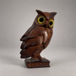 Escultura decorativa representando coruja, executada em madeira entalhada e polida.Medindo 9 x 6 cm, apresenta modelagem tridimensional das penas, asas e cabeça, com grandes olhos aplicados em tonalidades amarela e preta, criando contraste com a coloração castanha natural da madeira.