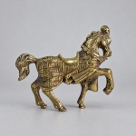 Escultura decorativa representando cavalo ricamente ajaezado, executada em metal de tonalidade dourada. Medindo 11 x 13 cm, apresenta corpo recoberto por ornamentação em relevo, com sela, arreios, cabeçada e demais elementos trabalhados em detalhe. A figura é representada em postura dinâmica, com uma das patas dianteiras elevada, pescoço arqueado e cauda recurvada.