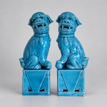 CÃES DE FÔ - Par de figuras decorativas representando os tradicionais leões guardiões chineses, conhecidos no Ocidente como cães de Fô. Medindo:11,5x5x3 cm cada, modelados em cerâmica e revestidos por esmalte azul-turquesa brilhante. As figuras aparecem sentadas sobre bases quadrangulares vazadas, com bocas abertas, presas aparentes e decoração em relevos e espirais.