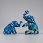 Conjunto composto por duas pequenas esculturas decorativas em cerâmica moldada e esmaltada em tonalidade azul-turquesa brilhante, representando elefantes com a tromba elevada. O maior mede 6,5 x 4,5 cm e o menor 3,5 x 5 cm. O exemplar maior apresenta postura mais dinâmica, com uma das patas dianteiras erguida, enquanto o menor possui composição mais compacta. As peças apresentam modelagem estilizada e bases ocas