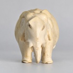 MARFIM - Pequena escultura decorativa representando elefante em posição de marcha, entalhada em marfim, com tromba recurvada, orelhas destacadas e detalhes anatômicos executados por incisões. Mede aproximadamente 5 x 8 cm. A superfície apresenta tonalidade marfim natural, leves marcas de manuseio e pequenas variações de coloração compatíveis com a natureza do material e com o uso.