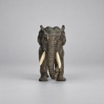 Escultura decorativa representando elefante, executada em bronze com pátina cinza-escura, apresentando modelagem naturalista, corpo maciço, orelhas destacadas, tromba recurvada e detalhes incisos sugerindo as pregas da pele. Medindo 6 x 9,5 cm, apresenta presas aplicadas em marfim e olhos destacados.