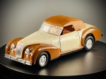 Miniatura Automóvel Clássico  Jaguar XK 120 (Escala 1:43), Apresenta uma elegante carroçaria de dois tons em creme e castanho metalizado, capota rígida amovível/imitando capota em tom castanho texturado, portas laterais móveis (abríveis) que revelam um interior detalhado em tons de castanho com tablier preto e instrumentos marcados, para-choques cromados e jantes raiadas desportivas. Med. 05x13x04 cm. Marcas do tempo e de uso.