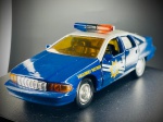 Miniatura Automóvel Clássico  Chevrolet Caprice Patrulha (Highway Patrol), Carroçaria bicolor em azul e branco, portas laterais móveis (abríveis), tejadilho equipado com sinaleiro luminoso de emergência (azul e vermelho), inscrições "Highway Patrol" e distintivos nas portas com estrela da polícia do Nevada, para-choques cromados e chassis inferior em plástico com gravação do fabricante (Road Champs Inc., 1993, West Caldwell, NJ). Med. 03x12x04 cm. Marcas do tempo e de uso.