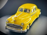 Miniatura Automóvel Clássico  DeSoto Custom Taxi (Escala 1:43), Carroçaria em tom amarelo vivo com detalhes gráficos característicos de táxi nas portas (faixa axadrezada e inscrições laterais), grelha frontal e para-choques cromados proeminentes, matrículas detalhadas de época e chassis gravado com a marca do fabricante (Vitesse, 1/43) e fabrico em Portugal (Fabriqué au Portugal). Marcas do tempo e de uso.