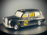 Miniatura Corgi  Austin London Taxi (Fairway / FX4), produzida pela consagrada marca Corgi, retratando o tradicional Austin London Taxi (o inconfundível táxi londrino FX4). ("CORGI" e "AUSTIN LONDON TAXI"), apresenta carroçaria na cor preta com portas laterais móveis (abríveis), revelando um detalhado interior em tons de amarelo/bege claro. Destaca-se pelos decalques laterais circulares característicos de rádio-táxi ("Rádio Taxis 272-0-272"), indicador de serviço luminoso no tejadilho e acabamentos cromados de época na grelha frontal, para-choques e jantes. Dimensões Aprox.: 4 x 12 x 5 cm. Marcas do tempo e de uso.