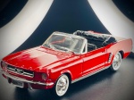 Miniatura Ford Mustang 1964 1/2 Cabriolet (Solido),  com carroçaria em tom vermelho vivo, grelha frontal detalhada com o emblema do cavalo selvagem, para-choques cromados, interior em tons escuros, capota recolhida simulada em preto e pneus clássicos com faixa branca e jantes raios de acabamento brilhante. O chassi inferior exibe as inscrições oficiais do fabricante.  Marcas do tempo e de uso.