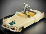 Miniatura Vitesse  Cadillac Conversível (Escala 1:43), miniatura fabricada em Portugal pela prestigiada marca Vitesse, retratando um clássico Cadillac conversível em tom creme.   O modelo destaca-se pela sua rica personalização temática de desfile oficial, incluindo duas figuras a bordo (condutor ao volante e figura em pé a saudar), pequenas bandeiras afixadas na dianteira (uma delas com o estandarte presidencial dos Estados Unidos) e acabamentos cromados de grande destaque. Na base inferior encontram-se gravadas as inscrições do fabricante ("Vitesse", "Cadillac", "1/43" e "Fabriqué au Portugal"). Marcas do tempo e de uso.