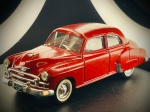 Miniatura Chevrolet 1950 (Sedan)  Solido (Escala 1:43), com carroçaria em tom vermelho vivo, acabamentos cromados de destaque (grelha frontal, para-choques e puxadores), pneus de banda branca com jantes coordenadas e chapa de matrícula detalhada do estado de Michigan (LZV-047). A base inferior encontra-se devidamente marcada com as inscrições do fabricante e especificações do modelo. Marcas do tempo e de uso.