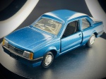 Miniatura Chevrolet Monza SL/E (Supermini Arpra)  Escala 1:43, om carroçaria em tom azul metalizado, portas laterais móveis (abríveis), interior detalhado em tons escuros com tablier e volante texturados, e placa traseira decorativa com a inscrição "TESTE QUATRO RODAS". Marcas do tempo e de uso.