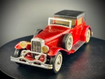 Miniatura 1930 Model "J" Duesenberg Town Car  Matchbox Models of Yesteryear, Carroçaria em tom vermelho metalizado com tejadilho rígido simulando lona preta, acabamentos e grelha dianteira cromados, faróis auxiliares amarelos, pneus com faixa branca e rodas sobressalentes montadas lateralmente. Inclui mala de viagem acoplada na traseira e pormenores mecânicos visíveis na base inferior em metal gravada. Med. 03x12x04 cm. Marcas do tempo e de uso.